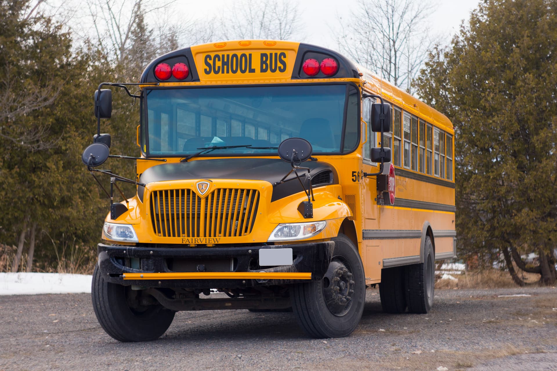 Close-up of an extended school bus stop arm with red flashing lights against a sky background.